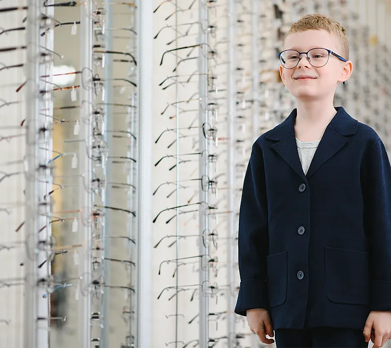 Kleiner Junge der sich in einem Spiegel anguckt und eine Brille anprobiert